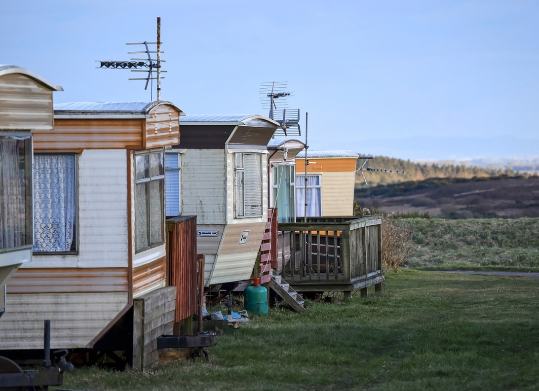En rad statiska husvagnar eller villavagnar placerade på gräsmark med utsikt över ett avlägset landskap.